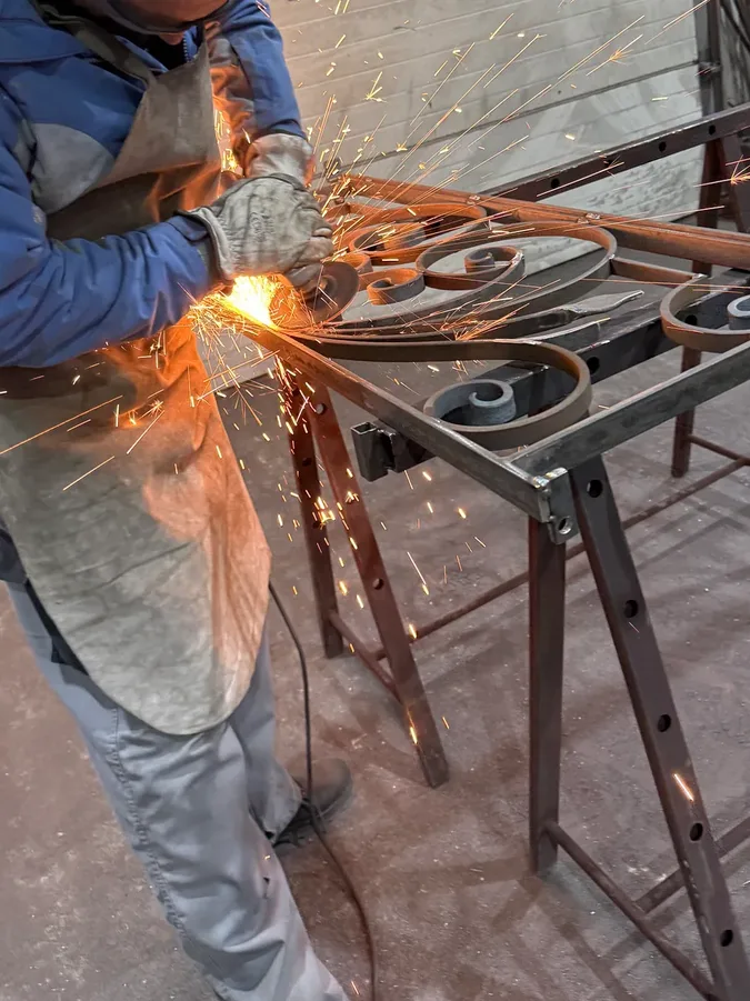 Forgeron meulant un ouvrage en fer forgé dans une gerbe d'étincelles, atelier L'Art de Faire