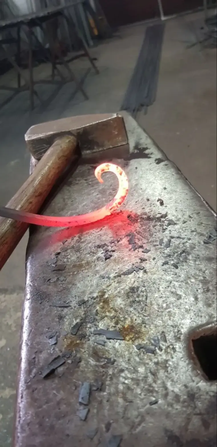 Volute en fer forgé rougie au feu sur enclume avec marteau, mise en forme à chaud, atelier L'Art de Faire