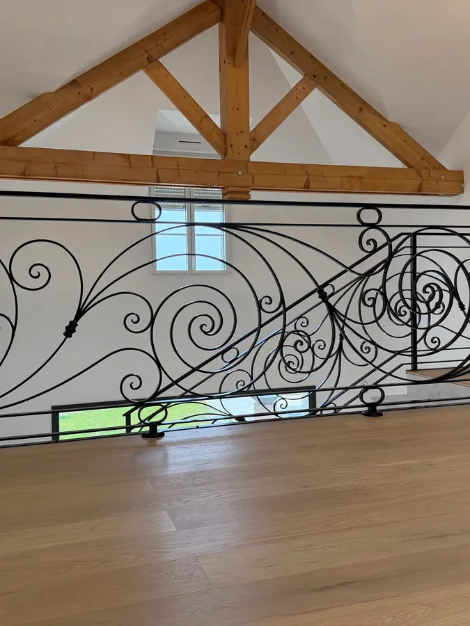 Garde-corps de mezzanine en fer forgé à spirales et volutes sous charpente bois apparente, parquet chêne, L'Art de Faire