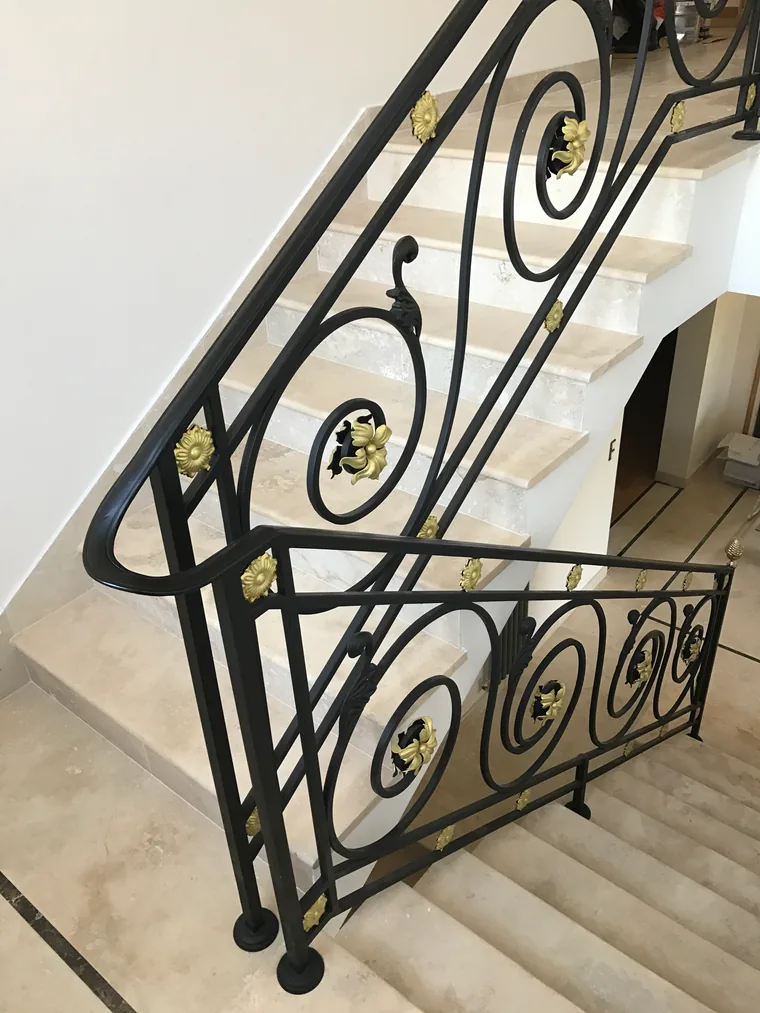 Rampe d'escalier intérieure en fer forgé à grandes volutes rehaussées de rosaces dorées, marches en pierre, L'Art de Faire
